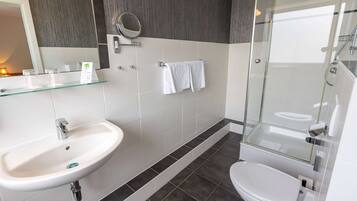 Un baño moderno con un lavamanos blanco, espejo e inodoro, y una ducha con mampara de vidrio.