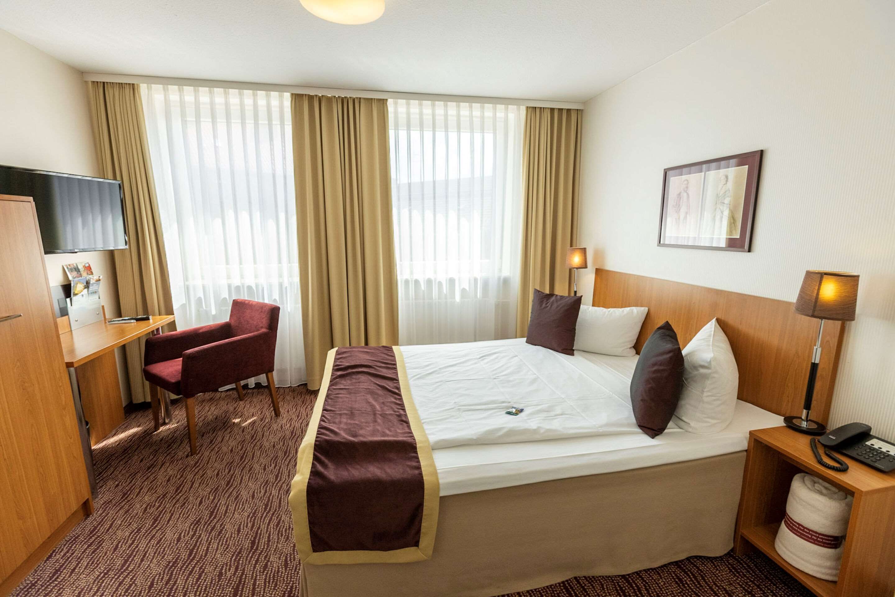 A hotel room with a bed, a desk, a chair, a television, and a lamp.