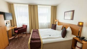 A hotel room with a bed, a desk, a chair, a television, and a lamp.