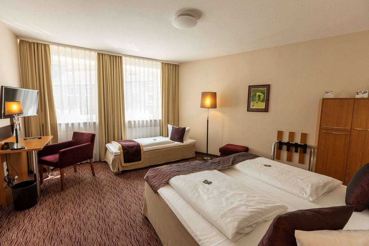 A hotel room with two beds, a desk with a computer, a chair, a TV, and a wardrobe.