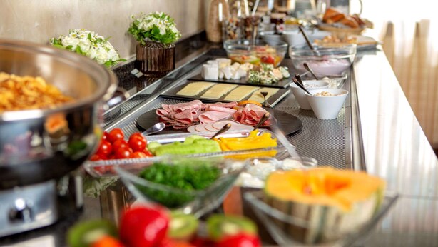 A buffet with various food items including meats, vegetables, and fruits. - Comfort Hotel Tom Kyle (Kiel)