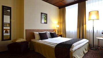 A hotel room with a large bed, a bedside table, a lamp, a mirror, and a window with curtains.