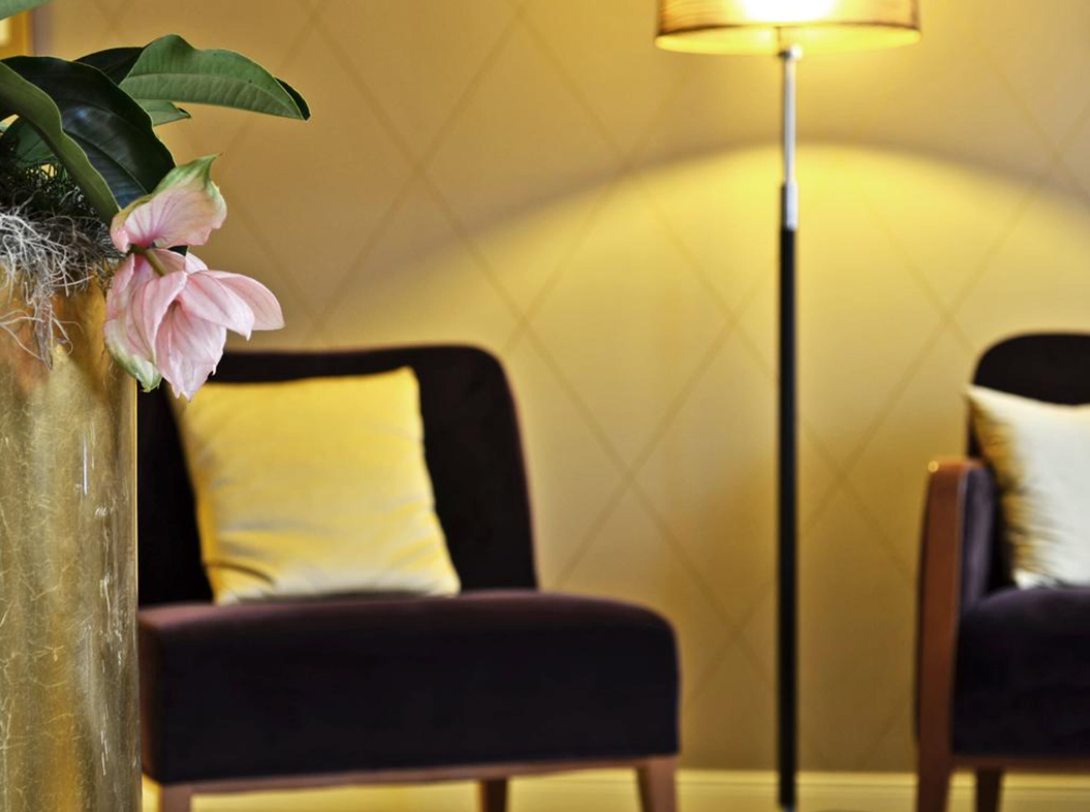 A room with a dark-colored armchair, a yellow pillow, and a floor lamp.
