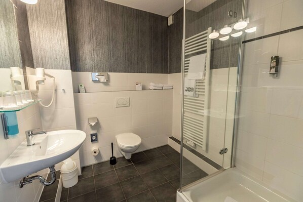 Un baño moderno con ducha envuelta en vidrio, un lavamanos blanco con accesorios cromados y un inodoro.