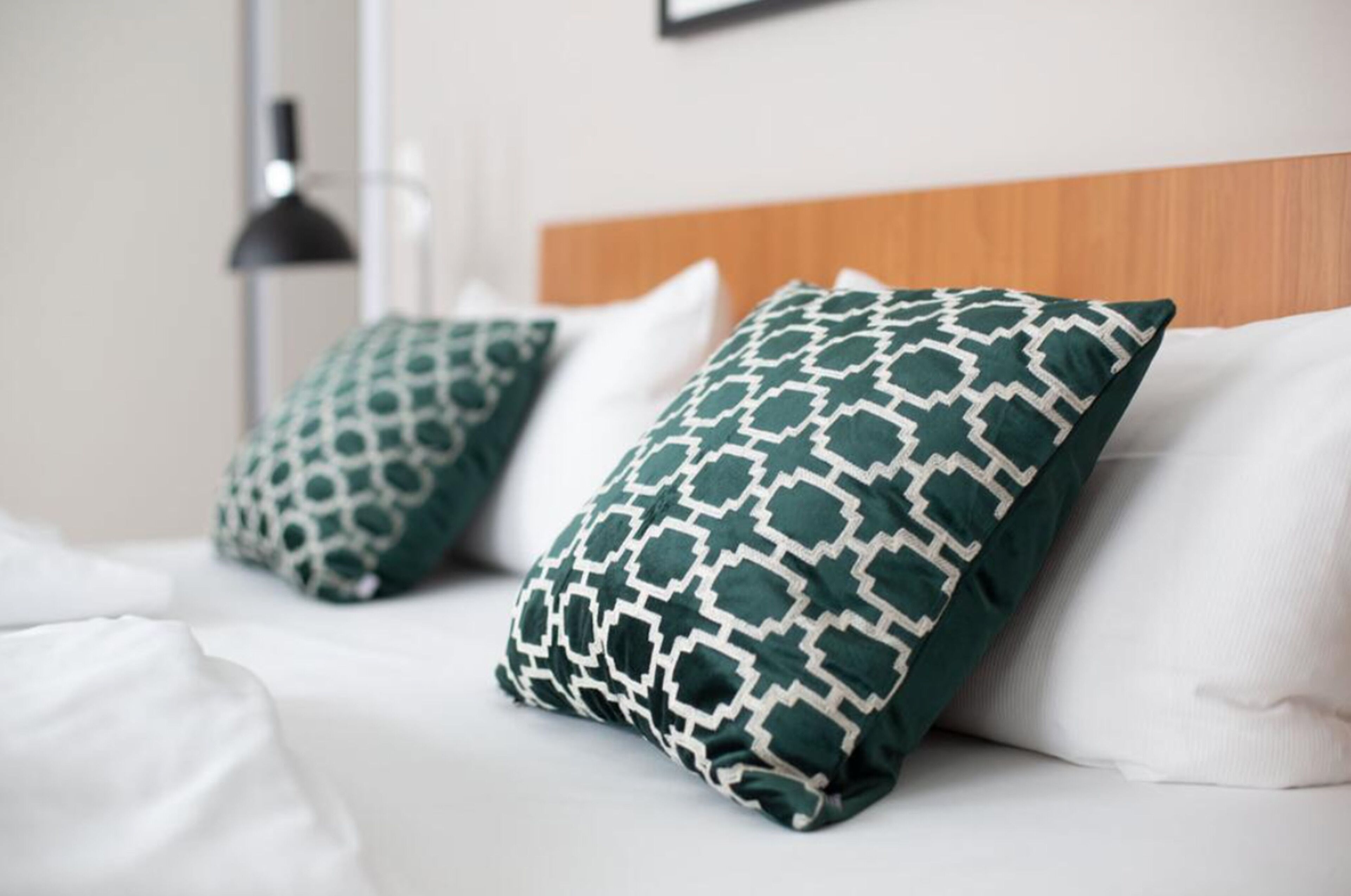 Una cama con ropa blanca y dos almohadas estampadas en verde.