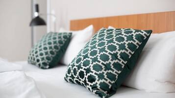 Una cama con ropa blanca y dos almohadas estampadas en verde.