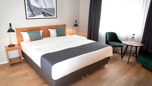 A hotel room with a large bed, two bedside lamps, a small table with a vase, a green armchair, and a framed picture on the wall. - Comfort Hotel Tom Kyle (Kiel)