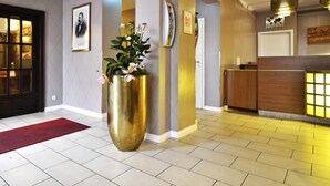 A hotel lobby with a reception desk, a large gold vase with flowers, and a red carpet. - Comfort Hotel Tom Kyle (Kiel)