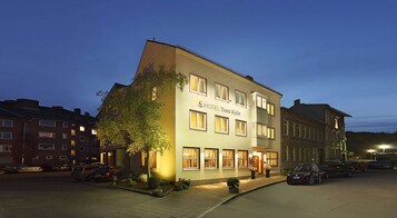 Un hotel llamado "HOTEL Tom Kyle" con una fachada moderna, múltiples ventanas y una entrada bien iluminada.