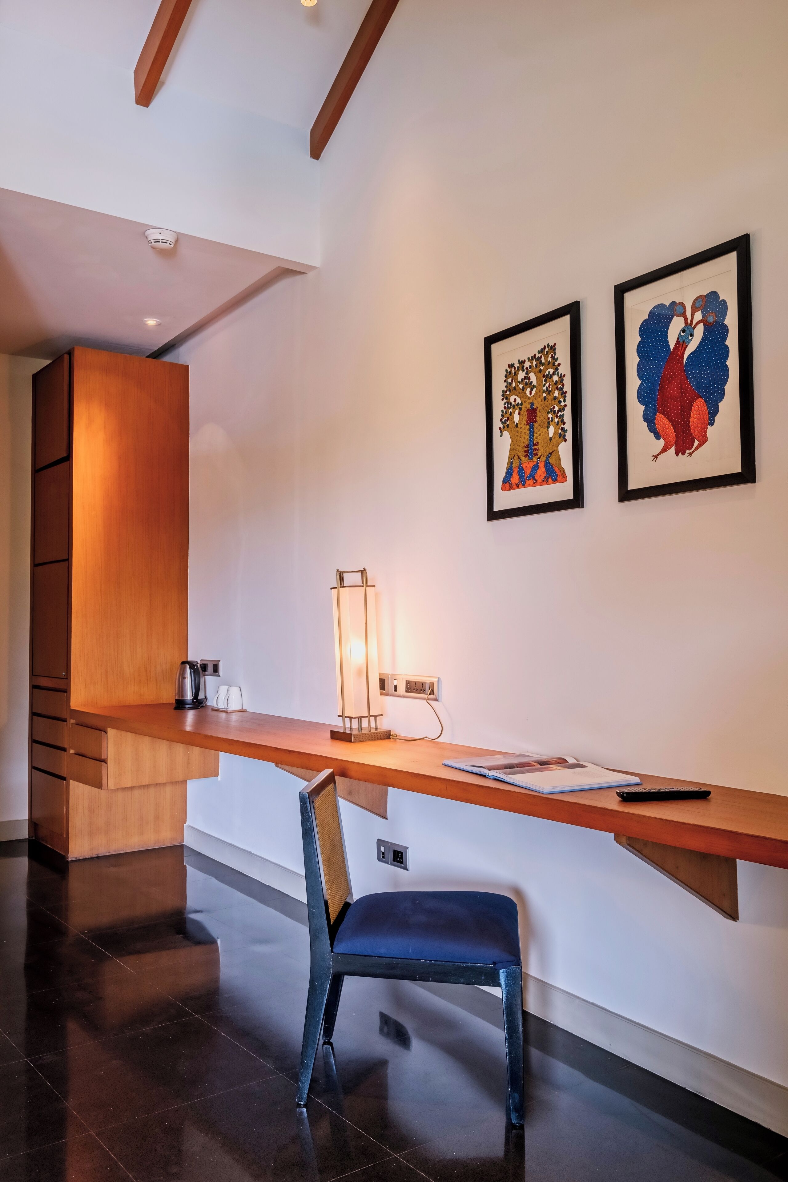 Una habitación moderna con un escritorio de madera, una silla azul y dos obras de arte enmarcadas en la pared.