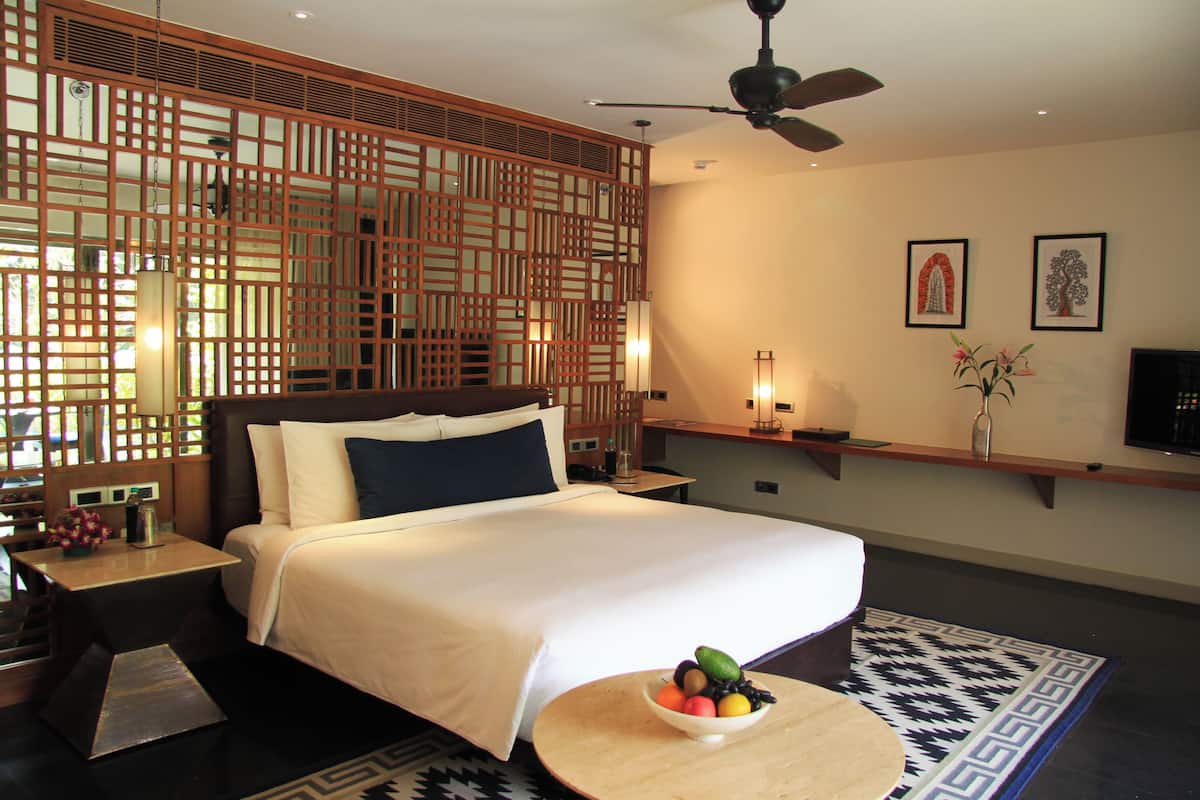 Een hotelkamer met een bed, nachtkastje en een fruitschaal op een klein rond tafeltje.