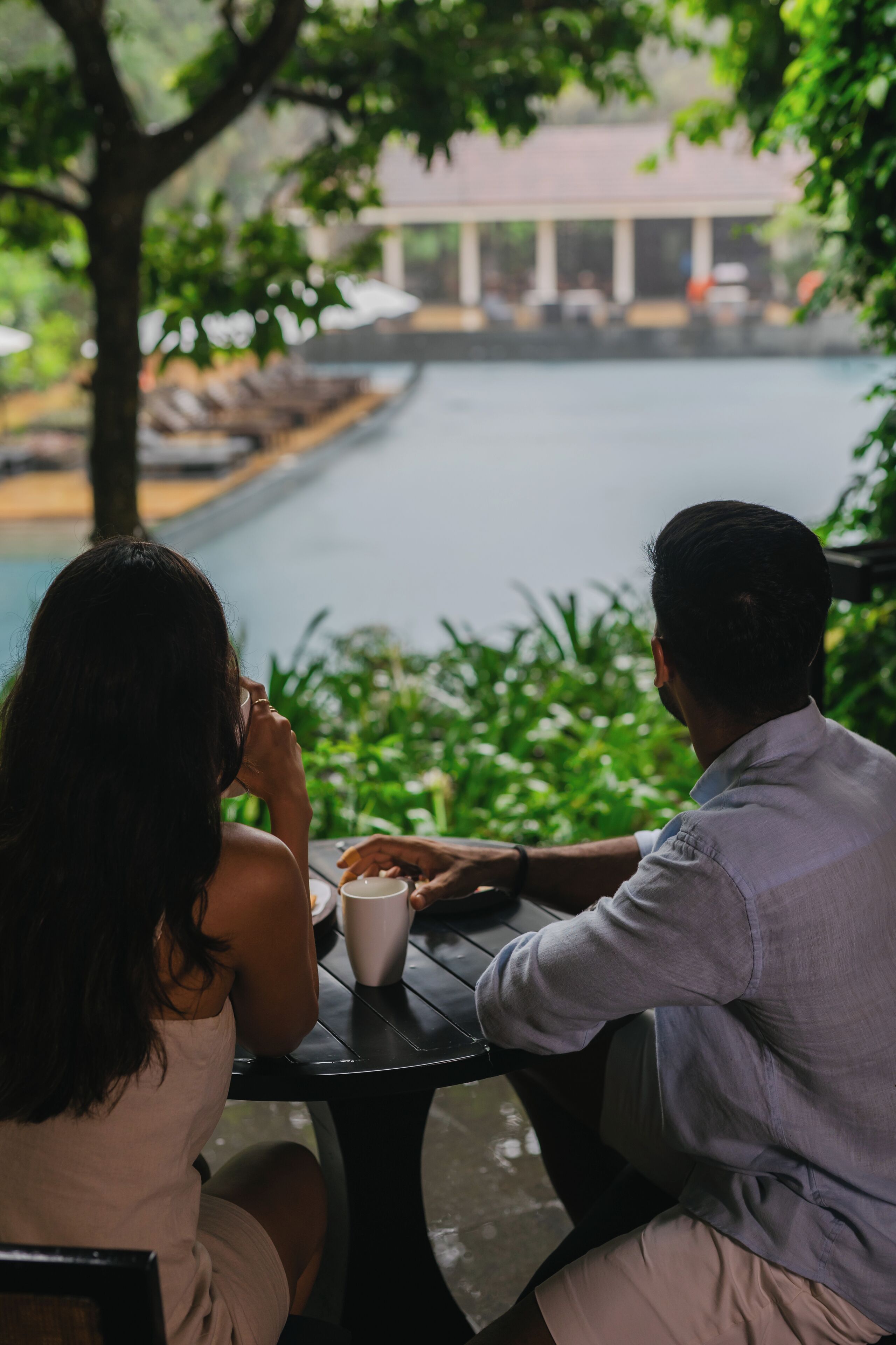 Two people sitting at a table with a view of a pool and greenery.