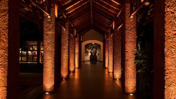 Un pasillo con columnas de piedra y vigas de madera que conduce a una estatua.