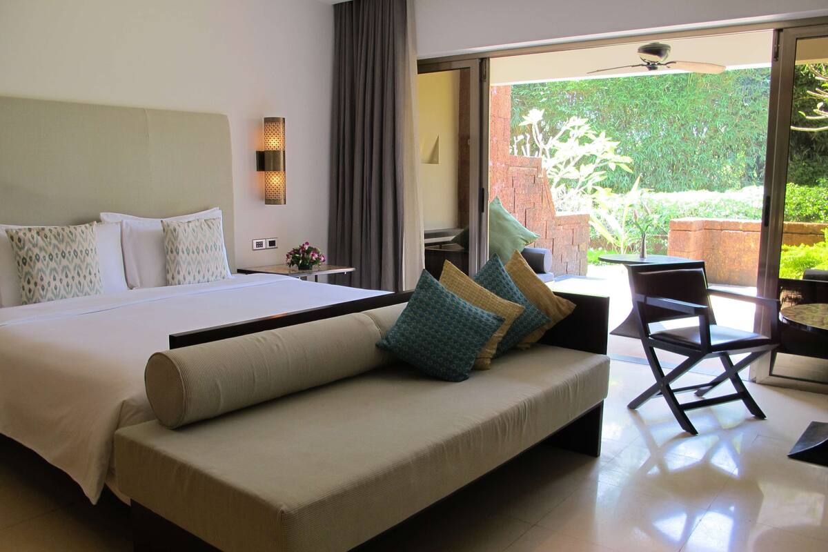 Een moderne hotelkamer met een groot bed, een sofa, een eethoek en uitzicht op groen.