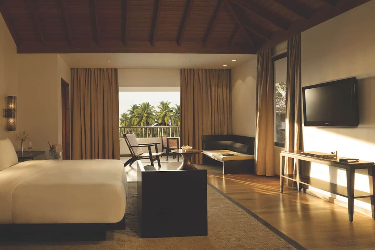 Een moderne hotelkamer met een groot bed, een bureau, een stoel, een televisie en een balkon met uitzicht op palmbomen.