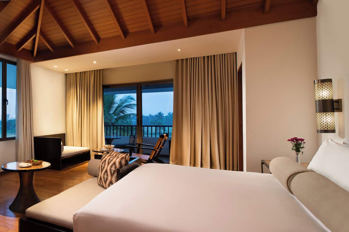 Een hotelkamer met een groot bed, een bank, een tafeltje, een stoel en een balkon met gordijnen.