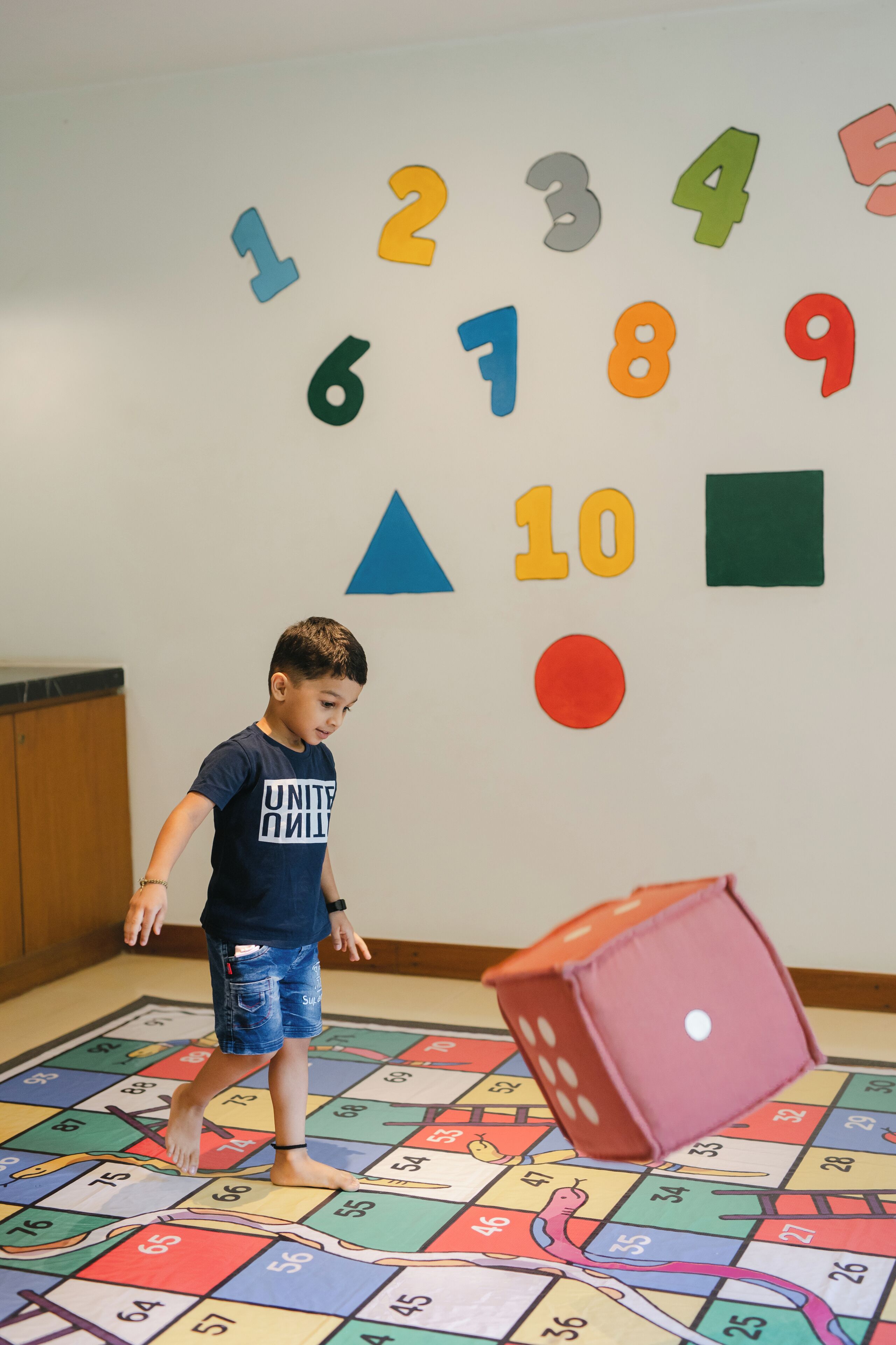 A child playing with a dice on a colorful board game mat.