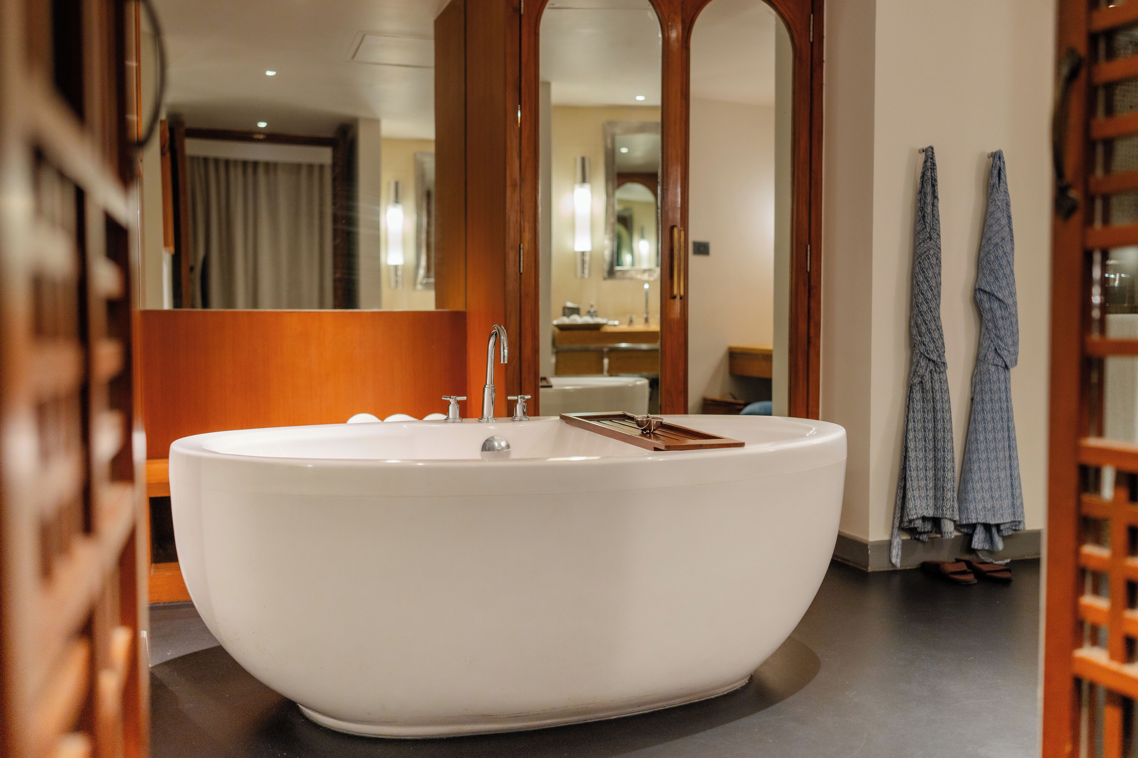 A large freestanding bathtub in a modern bathroom with a wooden vanity and a mirror.