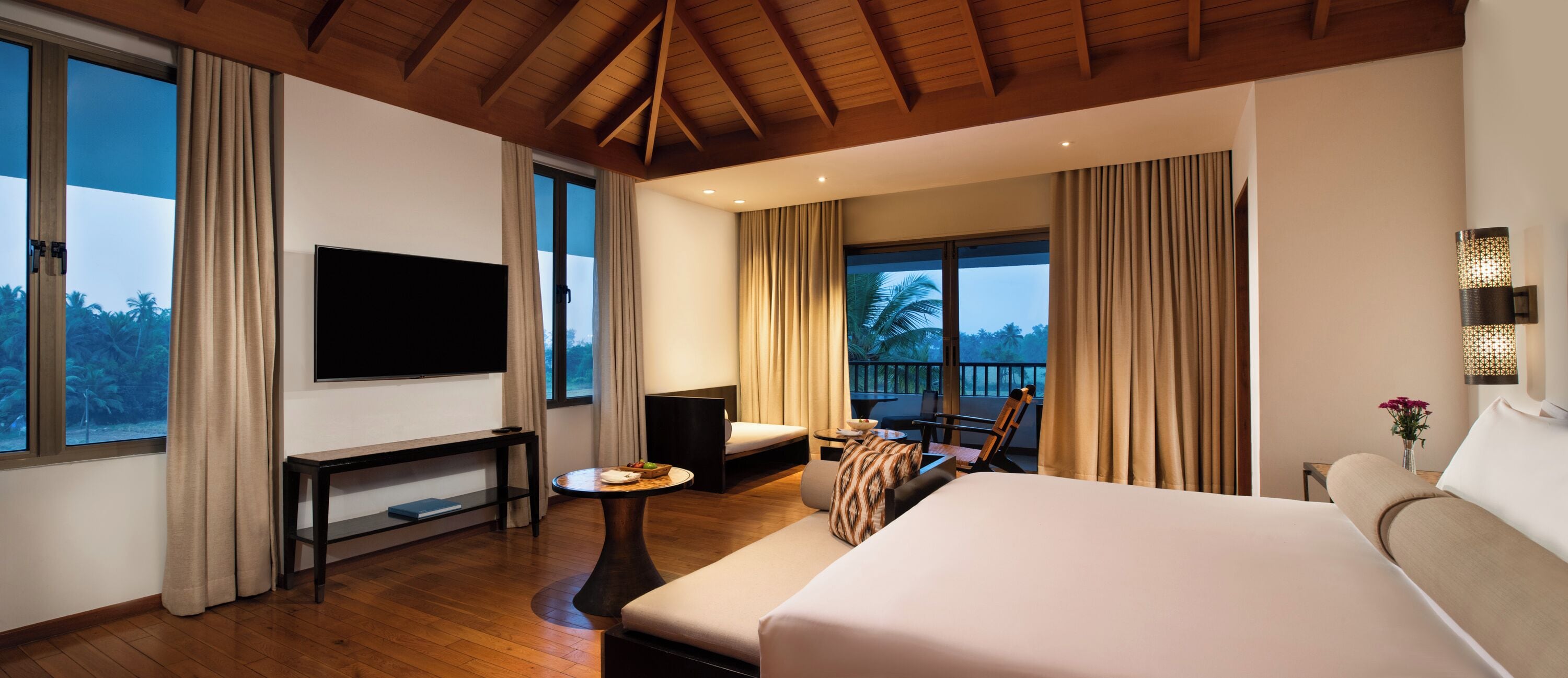 A hotel room with a large bed, a TV, a balcony with a chair, and a dining area.