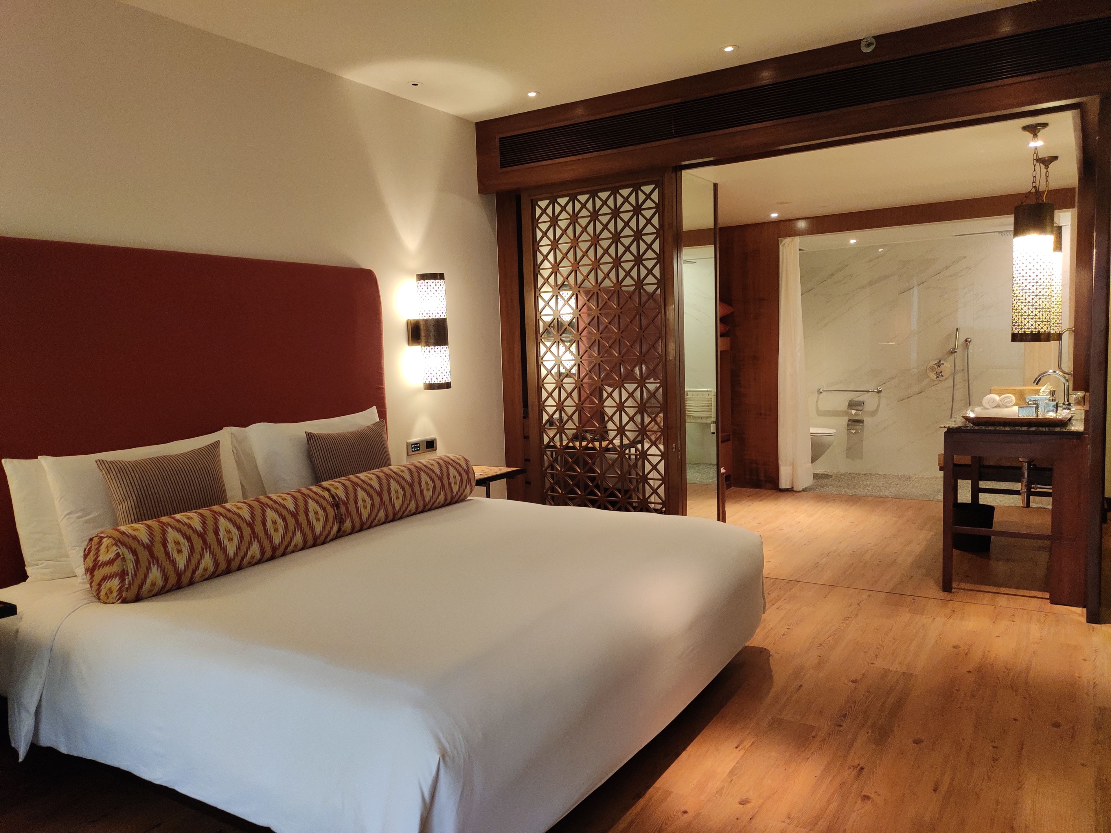 A hotel room with a large bed, wooden floor, and a view of the bathroom and staircase.