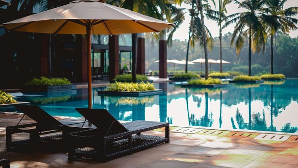 A poolside area with lounge chairs and an umbrella, surrounded by palm trees and a clear pool. - Alila Diwa Goa - A Hyatt Brand (Majorda)