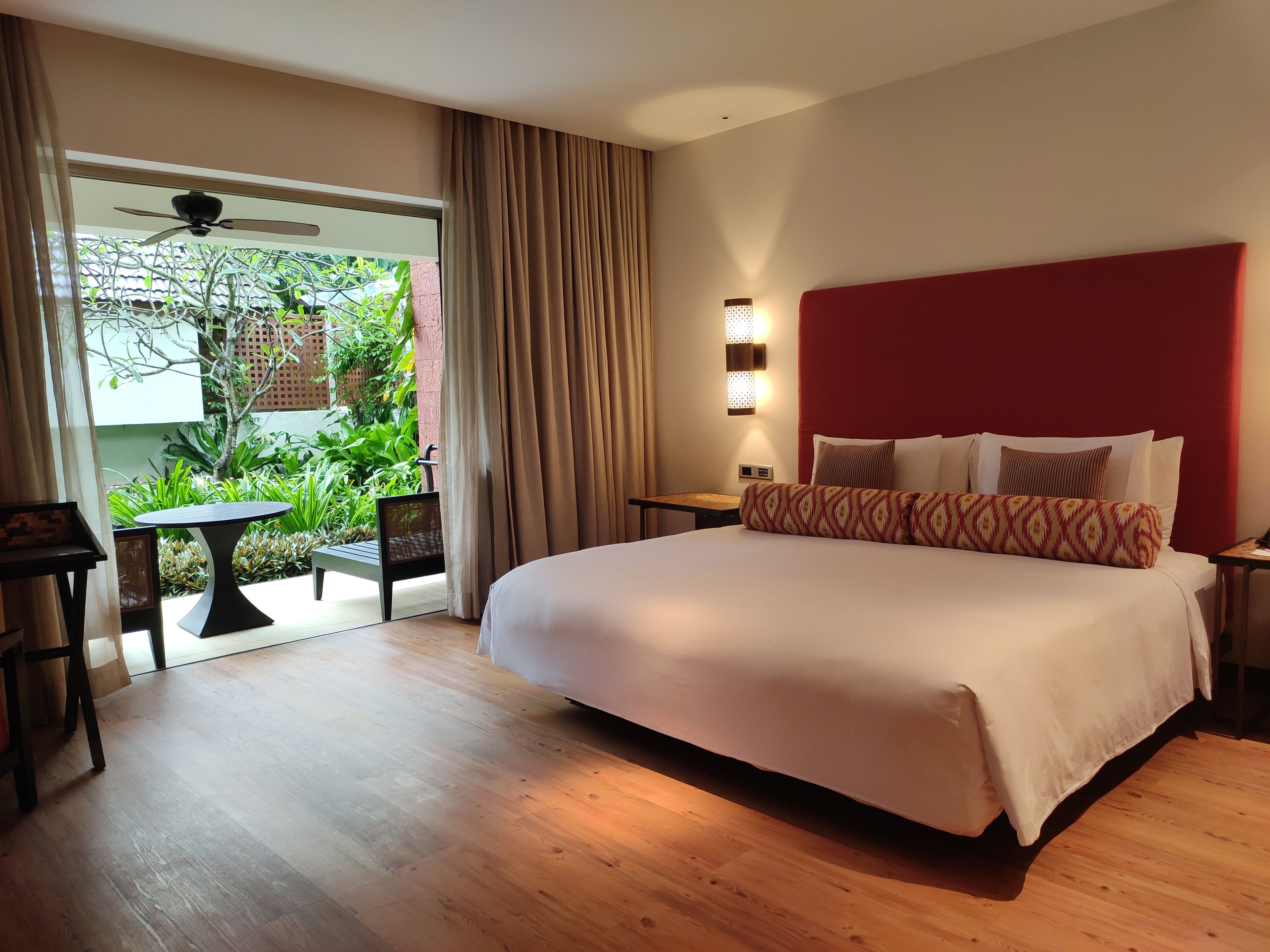 Habitación de hotel con una cama grande, una mesita, una silla, un ventilador de techo y vistas a zonas verdes.