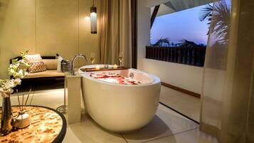 Un baño moderno con una bañera grande, un sofá y vistas a palmeras.