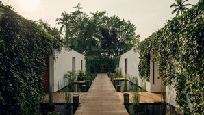 A wooden pathway leading to a white building with a sloped roof, surrounded by lush greenery and palm trees. - Alila Diwa Goa - A Hyatt Brand (Majorda)