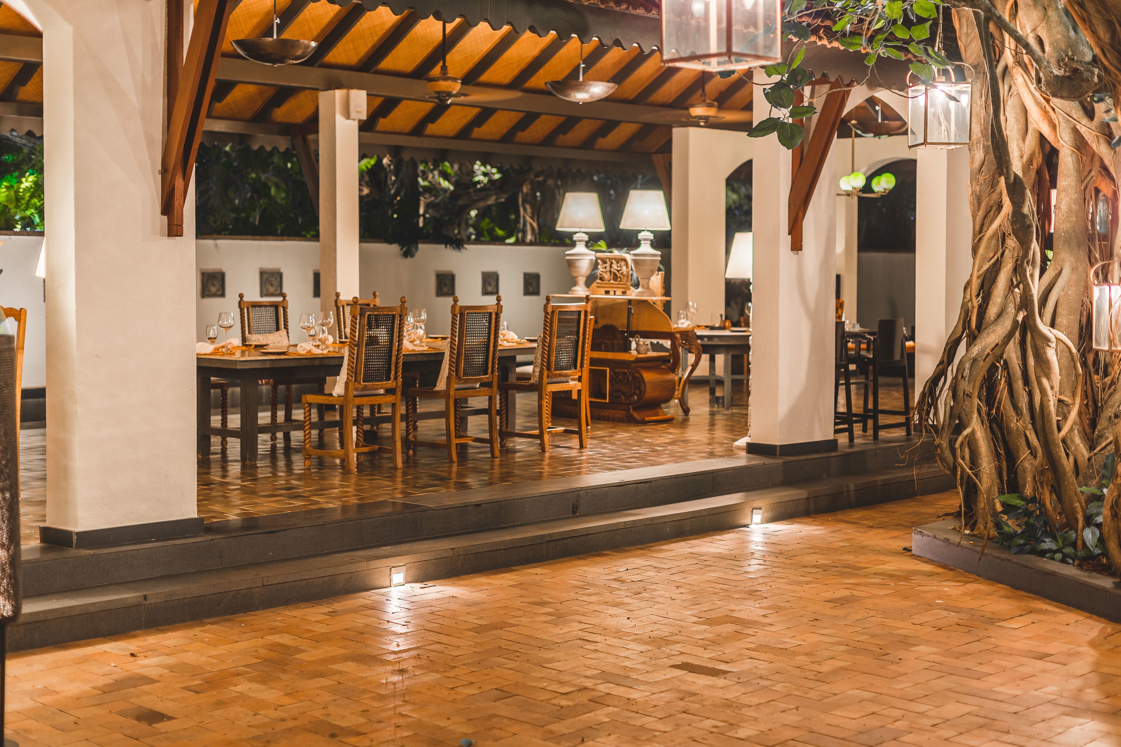 A restaurant with wooden flooring, tables, chairs, and hanging lamps.