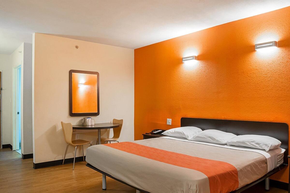 Habitación de hotel con una cama, un escritorio, dos sillas y una mesita de noche.