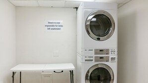 A laundry area with two LG commercial washers and a white table. A sign states 'Motel 6 is not responsible for items left unattended.'