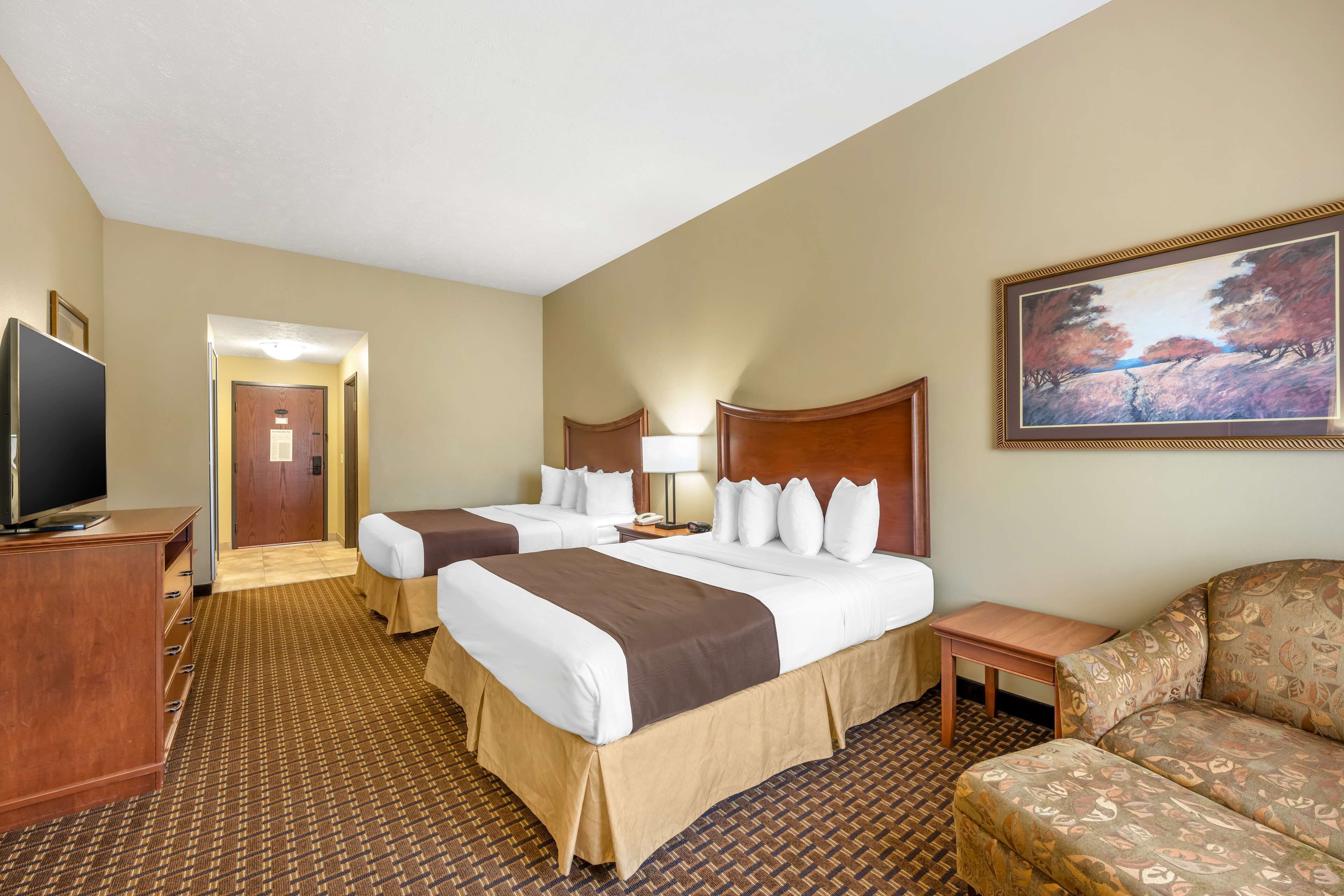 A hotel room with two beds, a TV, a desk, and a painting on the wall.