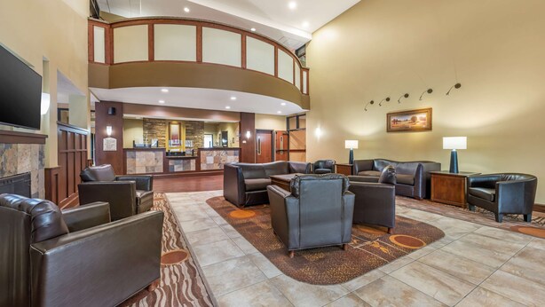 A hotel lobby with a curved wooden staircase, leather seating, a reception desk, and a large flat-screen TV. - Best Western Plus Grand Island Inn & Suites (Grand Island)