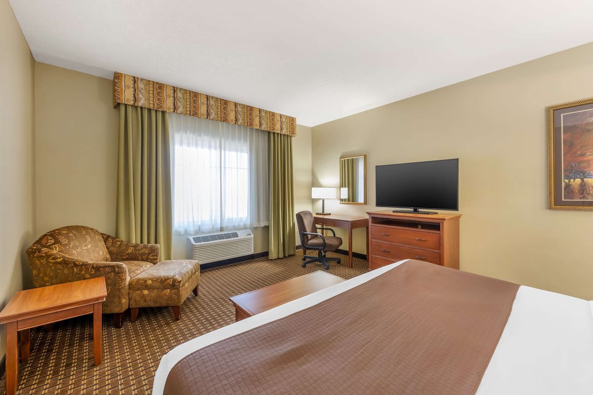 A hotel room with a bed, a desk, a chair, a television, and a window with curtains.