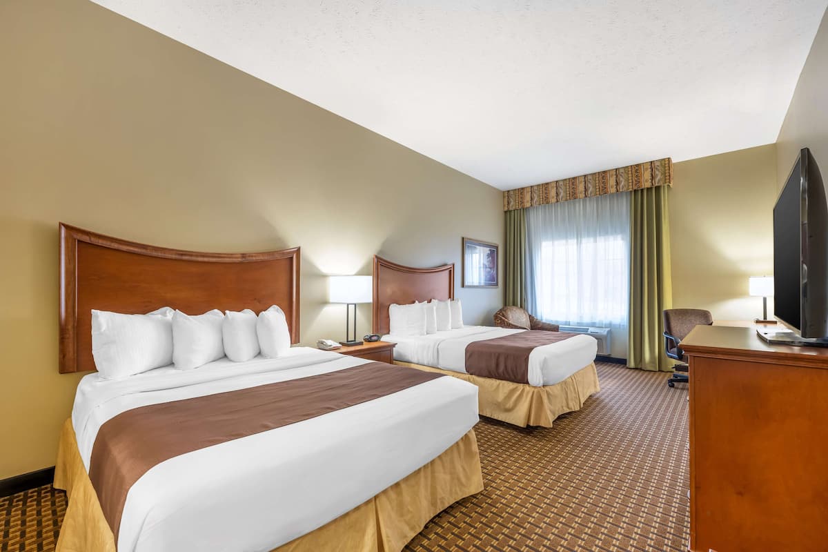 A hotel room with two beds, a desk, a television, and a window with curtains.