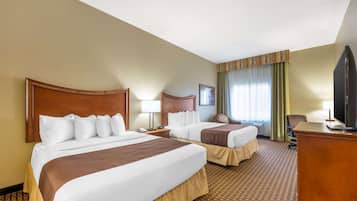 A hotel room with two beds, a desk, a television, and a window with curtains.