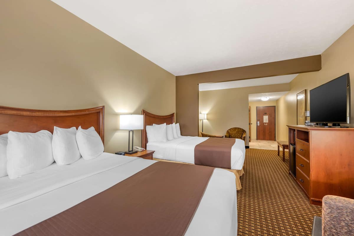 A hotel room with two beds, a television, a desk, and a chair.