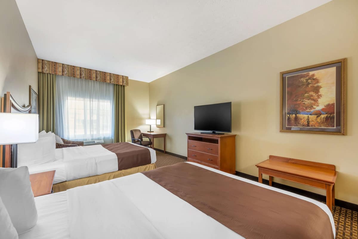 A hotel room with two beds, a television, a desk, and a painting on the wall.