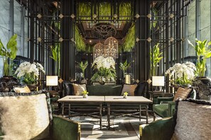 Un hall d’entrée luxueux avec un espace salon central, entouré de murs aux teintes sombres et de grandes fenêtres.