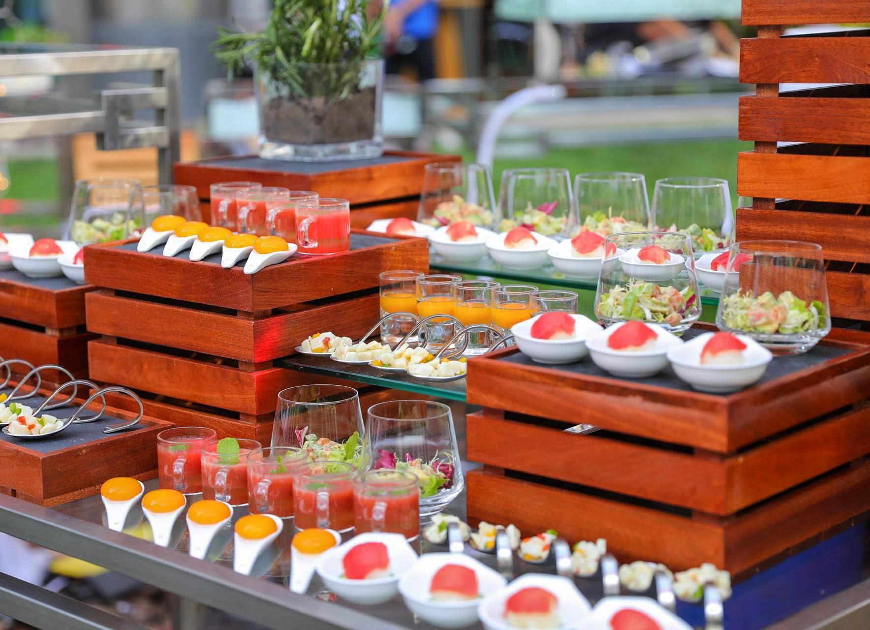 A buffet with various food items and drinks, including fruit skewers, salads, and juices, arranged on wooden tables.