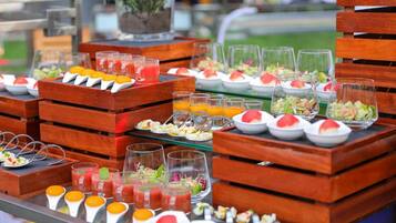 A buffet with various food items and drinks, including fruit skewers, salads, and juices, arranged on wooden tables.