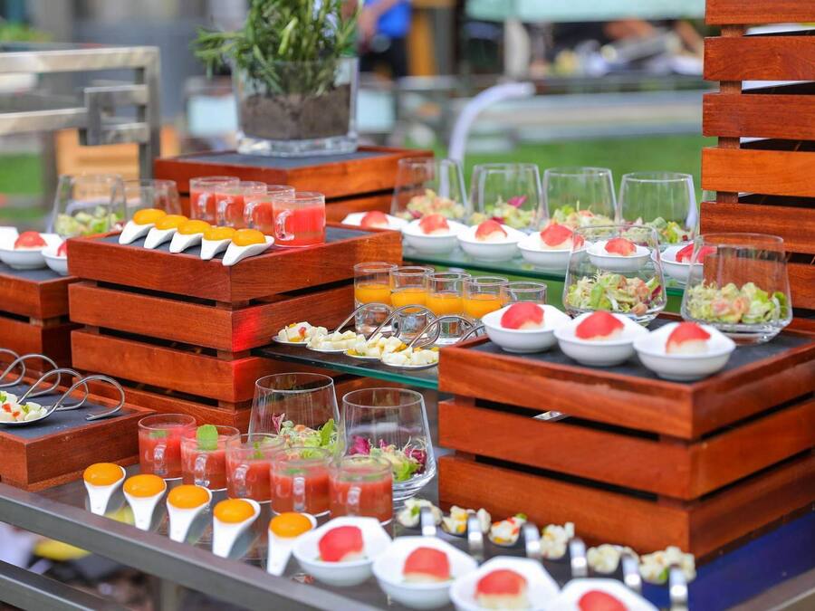 A buffet with various food items and drinks, including fruit skewers, salads, and juices, arranged on wooden tables.
