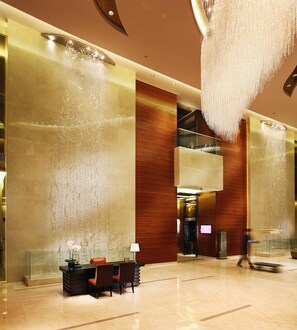 Eine Lobby mit einer Rezeption, Stühlen, einem Wasserspiel und einem modernen Kronleuchter.