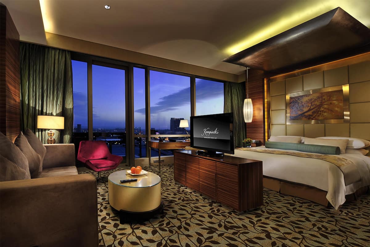 Habitación de hotel con una cama grande, televisión, escritorio y vistas a la ciudad al atardecer.