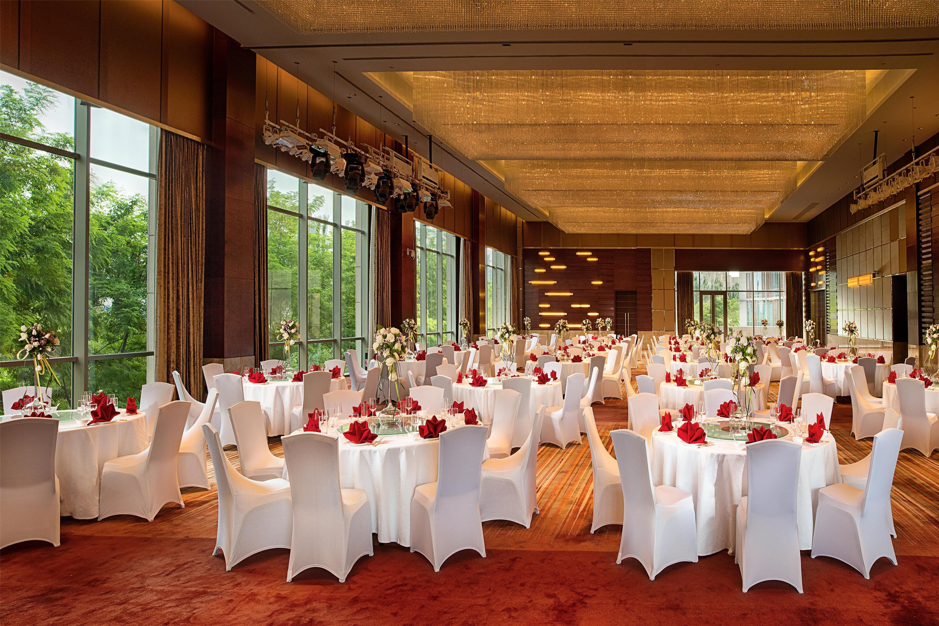 A large banquet hall with round tables, white chairs, and red centerpieces.