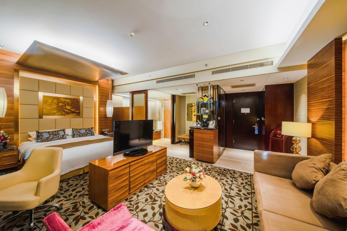 A modern hotel room with a large bed, a TV, a wooden coffee table, and a sofa.