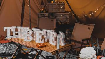 A tent interior with a table displaying illuminated letters spelling 'THERE BEER', a lantern, and a chair.