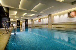 Una piscina con suelo de baldosas y escalera metálica.