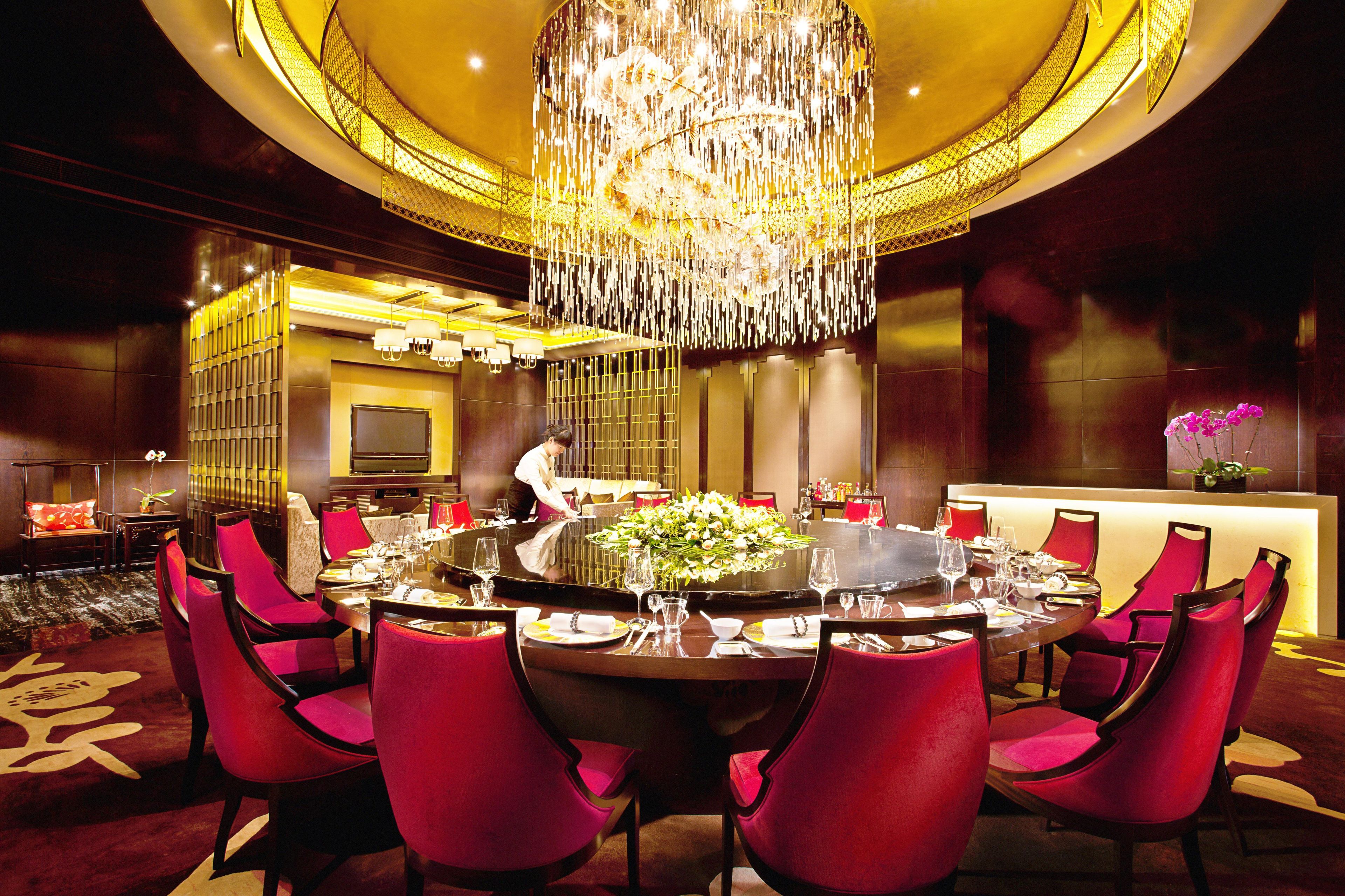 A dining area with a round table, red chairs, a chandelier, and a person serving.