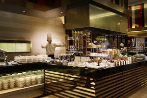 Un buffet avec plusieurs points de service, un chef qui prépare les plats et une variété de mets présentés sur des présentoirs à étages.
